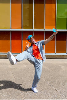 Joyful man dancing energetically in front of a multicolored windowed building - ADSF49496