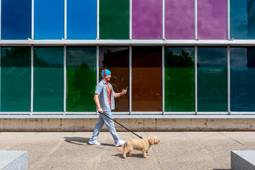 Man walking his dog past a multicolored glass building - ADSF49504