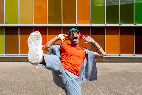 Joyful man dancing energetically in front of a multicolored windowed building - ADSF49505