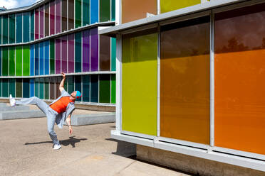 Joyful man dancing energetically in front of a multicolored windowed building - ADSF49506