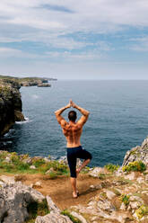 Man with hands in a yoga pose overlooking a vast ocean from a rocky cliff, accompanied by a dog. - ADSF49510