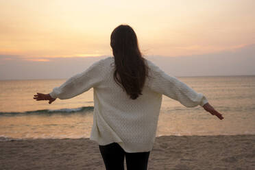 Young woman standing with arms outstretched at beach - AAZF01242