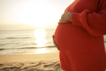 Schwangere Frau mit Händen auf dem Bauch am Strand - AAZF01257