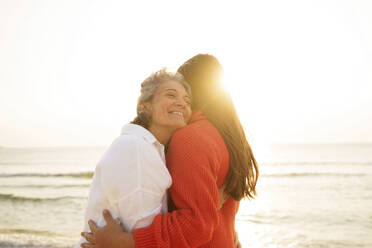 Loving mother hugging daughter at beach - AAZF01265