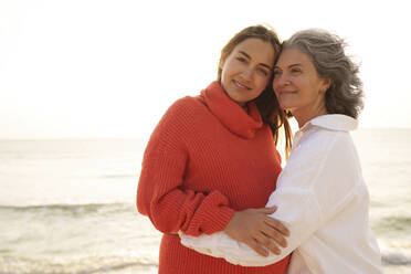 Happy mother embracing pregnant daughter at beach - AAZF01274