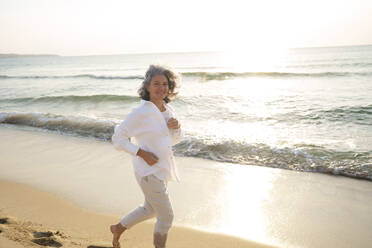 Smiling mature woman running at beach - AAZF01277