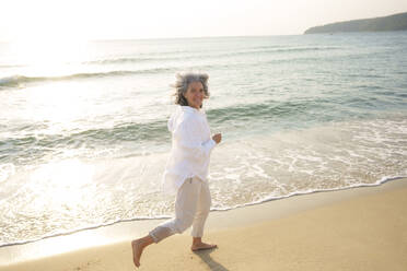 Glückliche reife Frau läuft am Strand - AAZF01278