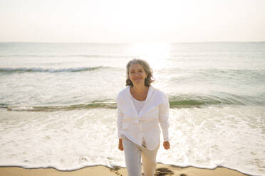 Smiling mature woman walking in front of sea at beach - AAZF01287