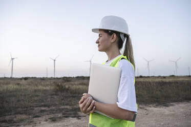 Nachdenklicher Ingenieur, der einen Laptop hält und vor einem Feld steht - ALKF00852