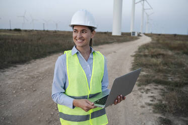 Glücklicher Ingenieur mit Laptop auf einem Windkraftanlagenfeld - ALKF00858