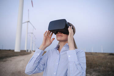 Smiling engineer wearing virtual reality simulators at wind turbines field - ALKF00867