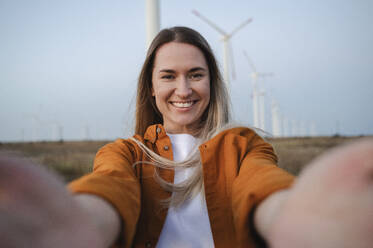 Smiling woman taking selfie in front of wind turbines - ALKF00871