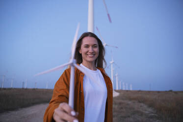 Glückliche Frau hält Modell einer Windkraftanlage auf einem Feld - ALKF00879