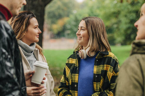 Smiling family holding coffee cups and talking in park - VSNF01464