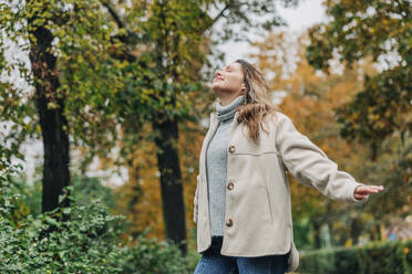 Carefree young woman with eyes closed in autumn park - VSNF01470