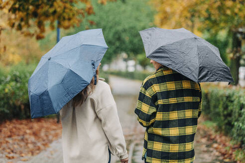 Mutter und Tochter halten Regenschirme und gehen im herbstlichen Park spazieren - VSNF01472