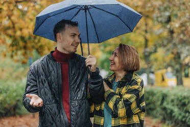 Glückliche Mutter mit Sohn, der einen Regenschirm hält und sich im Herbst im Park unterhält - VSNF01473