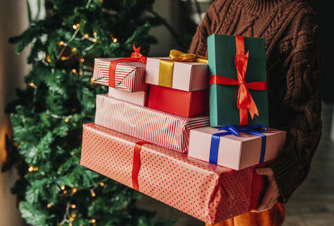 Frau hält verschiedene Geschenke in der Nähe von Weihnachtsbaum zu Hause - VSNF01480