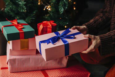 Hands of woman stacking gifts near Christmas tree at home - VSNF01484