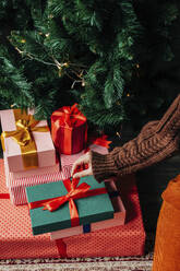 Hand of woman arranging gifts near Christmas tree at home - VSNF01489