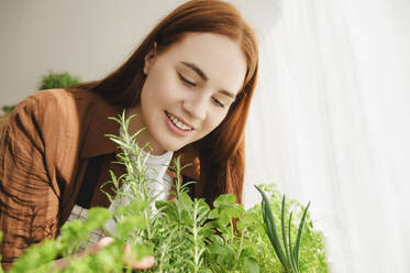 Smiling redhead botanist admiring plants at home - ALKF00904