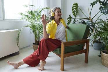Lächelnde Frau mit drahtlosen Kopfhörern beim Yoga auf einem Stuhl zu Hause - AAZF01311