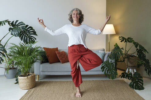 Smiling woman practicing yoga standing on one leg at home - AAZF01318