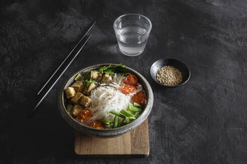 Bowl of vegan Tom kha kai soup with tofu, tomatoes, salad, rice noodles, sesame seeds and scallion - EVGF04420