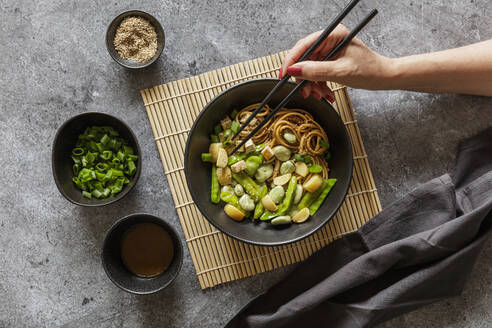 Hand einer Frau, die eine vegane Miso-Udon-Schüssel mit Tofu, Zuckerschoten, Saubohnen und Rüben isst - EVGF04422