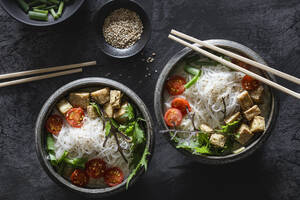 Schalen mit veganer Tom kha kai-Suppe mit Tofu, Tomaten, Salat, Reisnudeln, Sesam und Frühlingszwiebeln - EVGF04423