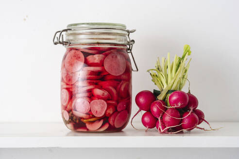 Jar with pickled radish near vegetables on shelf at home - TILF00026