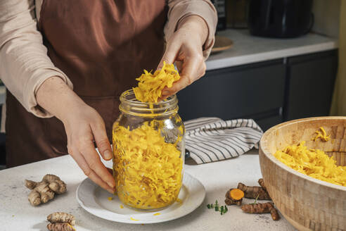 Frau legt Sauerkraut in Glasgefäß an Küchentisch - TILF00027