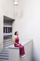 Woman sitting with eyes closed on wall near staircase - JSMF02952