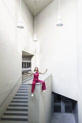 Woman sitting with arms raised on wall near staircase - JSMF02956