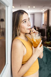 Woman sipping iced tea through straw at home - DSIF00730