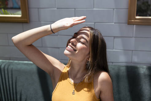 Smiling woman shielding eyes from sunlight at home - DSIF00731