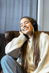 Smiling woman listening to music through wireless headphones at home - DSIF00732