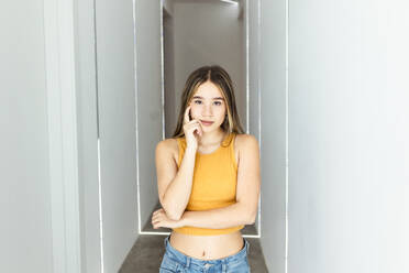 Young woman touching face and standing in corridor at home - DSIF00738