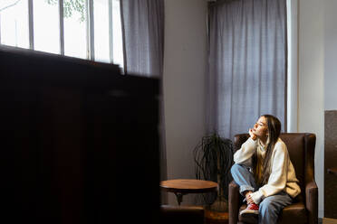 Frau mit geschlossenen Augen sitzt zu Hause auf einem Sessel - DSIF00747