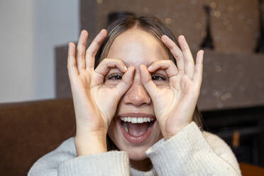 Cheerful woman gesturing OK sign over face at home - DSIF00748