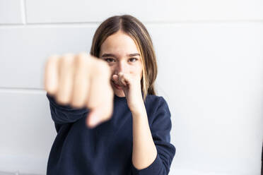 Young woman punching in front of wall at home - DSIF00754