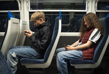 Boy and girl using smart phones sitting in train - NJAF00623