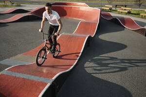 Man riding BMX bike on sports track in park - MRPF00025