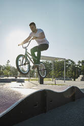 Man doing stunt with BMX bike on sports track in park - MRPF00026
