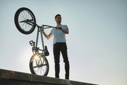 Mann hält BMX-Rad und steht an der Wand unter dem Himmel - MRPF00028