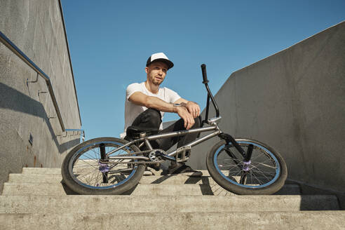 Thoughtful man sitting with BMX bike on staircase - MRPF00035