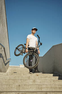 Mann stehend mit BMX-Rad auf Treppe unter Himmel - MRPF00036