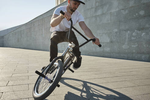 Mann macht Stunt mit BMX-Rad vor einer Mauer an einem sonnigen Tag - MRPF00040