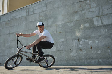 Mann mit Mütze und Stunt mit BMX-Rad vor einer Wand - MRPF00041