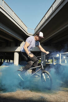 Mann fährt BMX-Rad und stößt in der Nähe einer Brücke blauen Rauch aus - MRPF00051